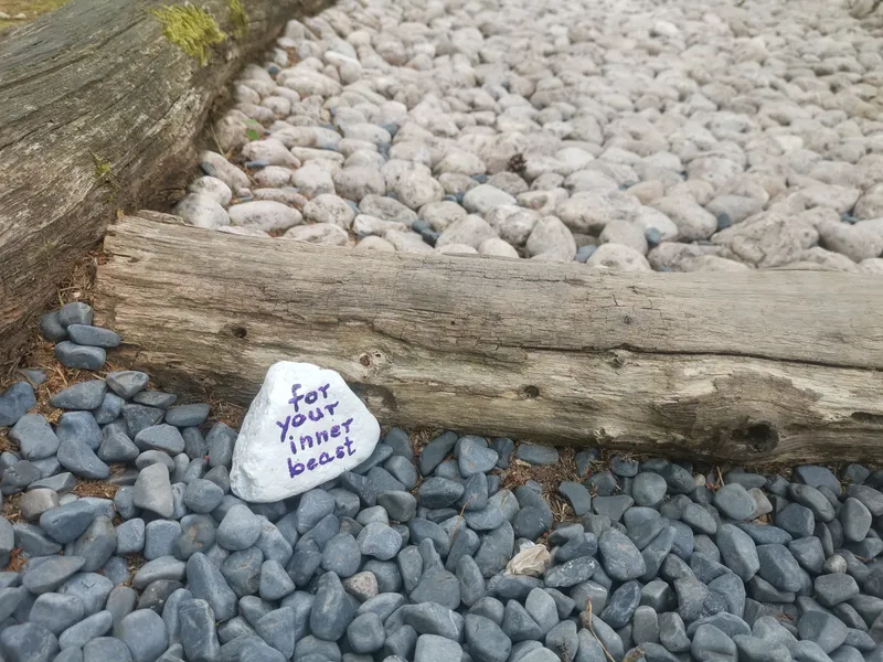 Ein heller Stein an einer räumlichen Trennung mit einem Holzstamm zwischen zwei verschiedenen Steinböden mit der Aufschrift in blauer Farbe: "for your inner beast"